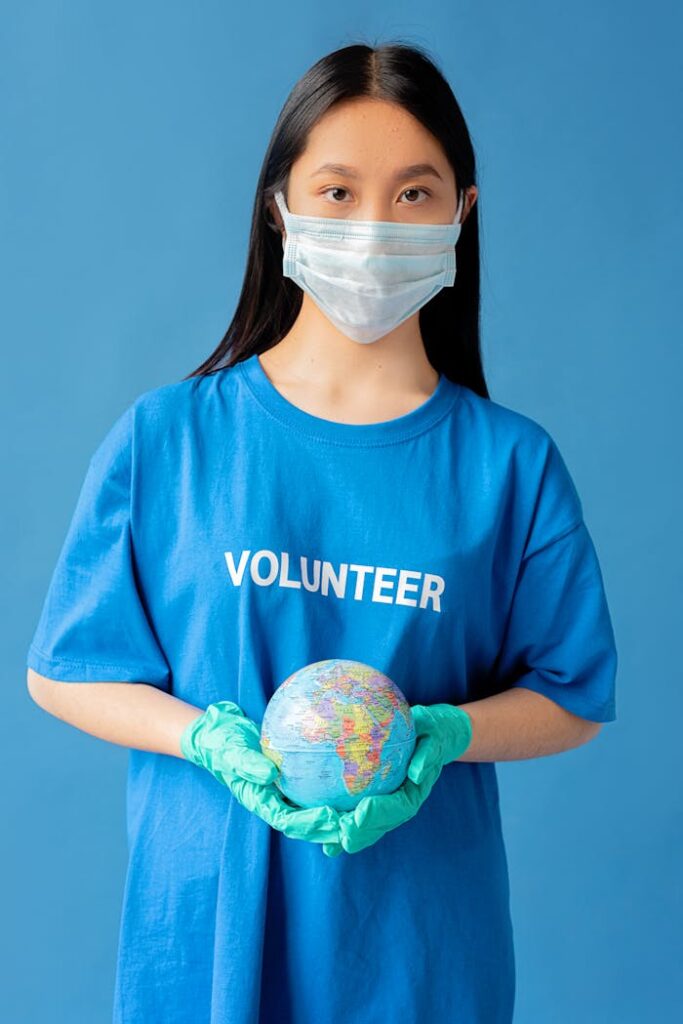 Woman wearing mask and gloves holds a globe, symbolizing global volunteer work.